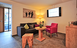 Gemütlicher Empfangsbereich mit Sofa, Schreibtisch, Fernseher und rotem Teppich auf der Treppe in einer modernen Unterkunft.