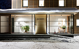 Glasfront des Das Tannberg bei Nacht mit beleuchtetem Eingangsbereich, Pflanzen, Schnee und Holzverkleidung.