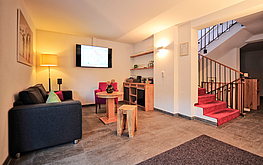 Gemütlicher Empfangsbereich mit Sofa, Schreibtisch, Fernseher und rotem Teppich auf der Treppe in einer modernen Unterkunft.