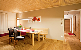 Große Wohnküche mit Holz-Eckbank, Esstisch, zwei Stühlen, Hängelampe, Mohnblumenbild und Blick zum Flur.