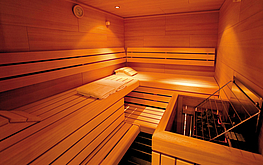 Holzsauna mit finnischem Ofen, gestuften Holzliegen, Kopfkissen und warmer, indirekter Beleuchtung.