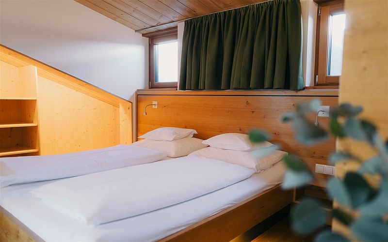 Doppelbett mit Holz-Kopfteil und Dachschräge in einem Apartment von Das Tannberg